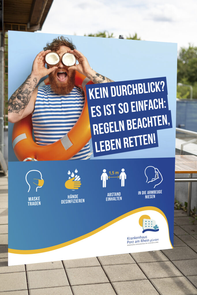 Mann mit Schwimmring auf Rollup mit Kokosnüssen auf den Augen, Aktion zum Corona Schutz Krankenhaus Köln-Porz